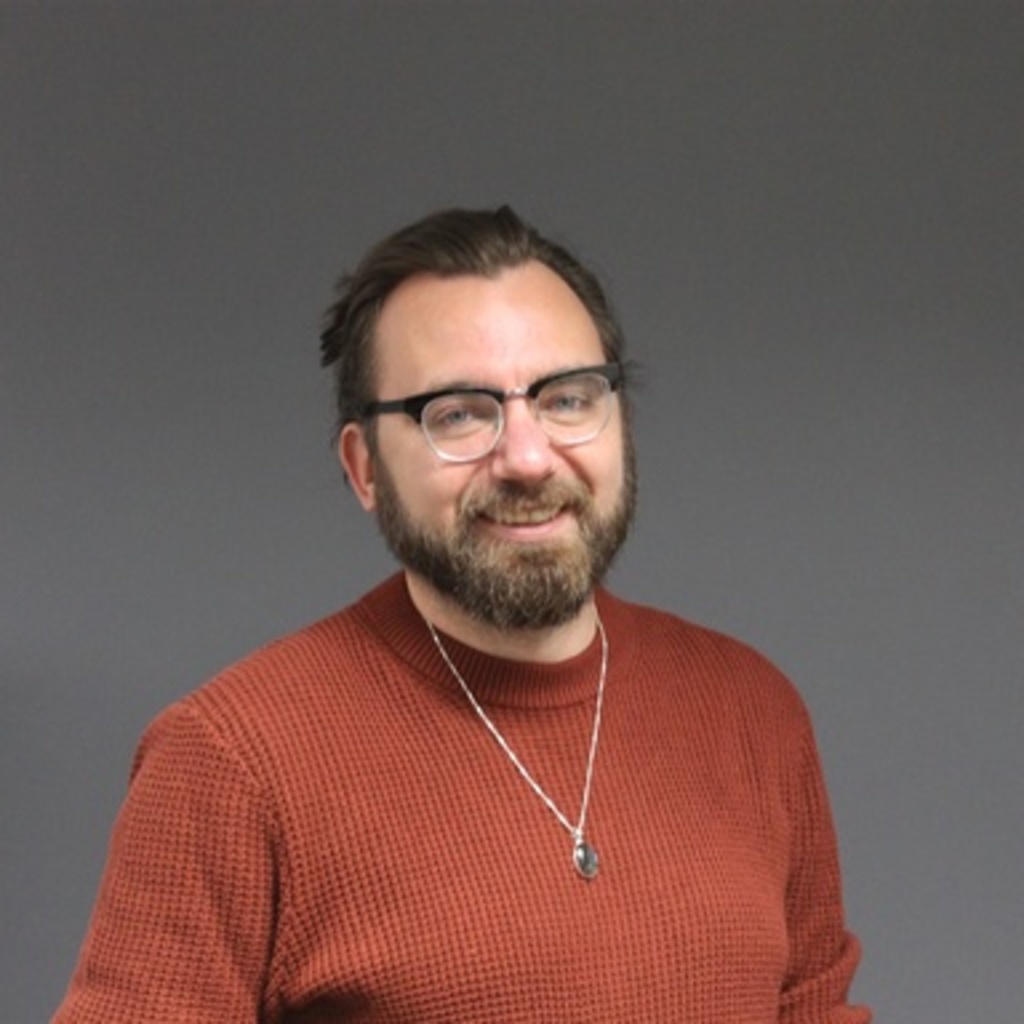 young man with hair back and glasses, wearing an orange shirt