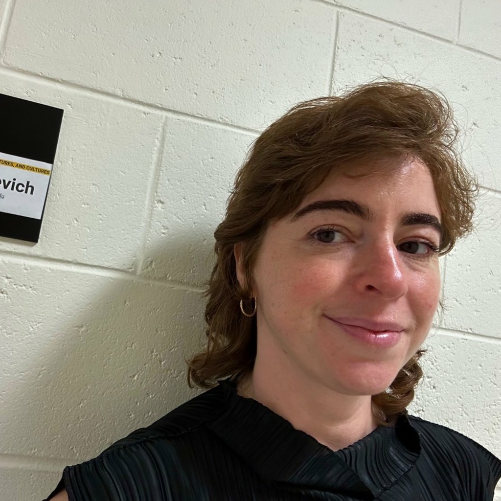 picture of woman with medium-length brown hair in a black shirt standing against a wall